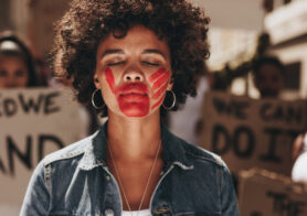 Woman with a hand print on her mouth, demonstrating violence on women. Woman protesting against domestic violence with group in background.